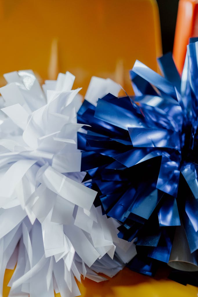 Close-up of white and blue pom-poms on a vibrant orange background, perfect for cheerleading themes.